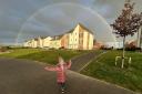 Three-year-old Lola smiles while standing underneath a rainbow over a housing estate in a Grove neighbourhood.