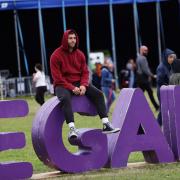 A festival goer sat on a big vegan sign at Vegan Campout Festival, in Bicester