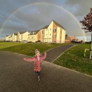 Three-year-old Lola smiles while standing underneath a rainbow over a housing estate in a Grove neighbourhood.